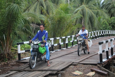 Sarwaji dan Mansur dengan nyaman membawa kelapa hasil kebun mereka melintasi Jembatan Handil Samsu yang diperbaiki melalui kegiatan TMMD Reguler ke-109.